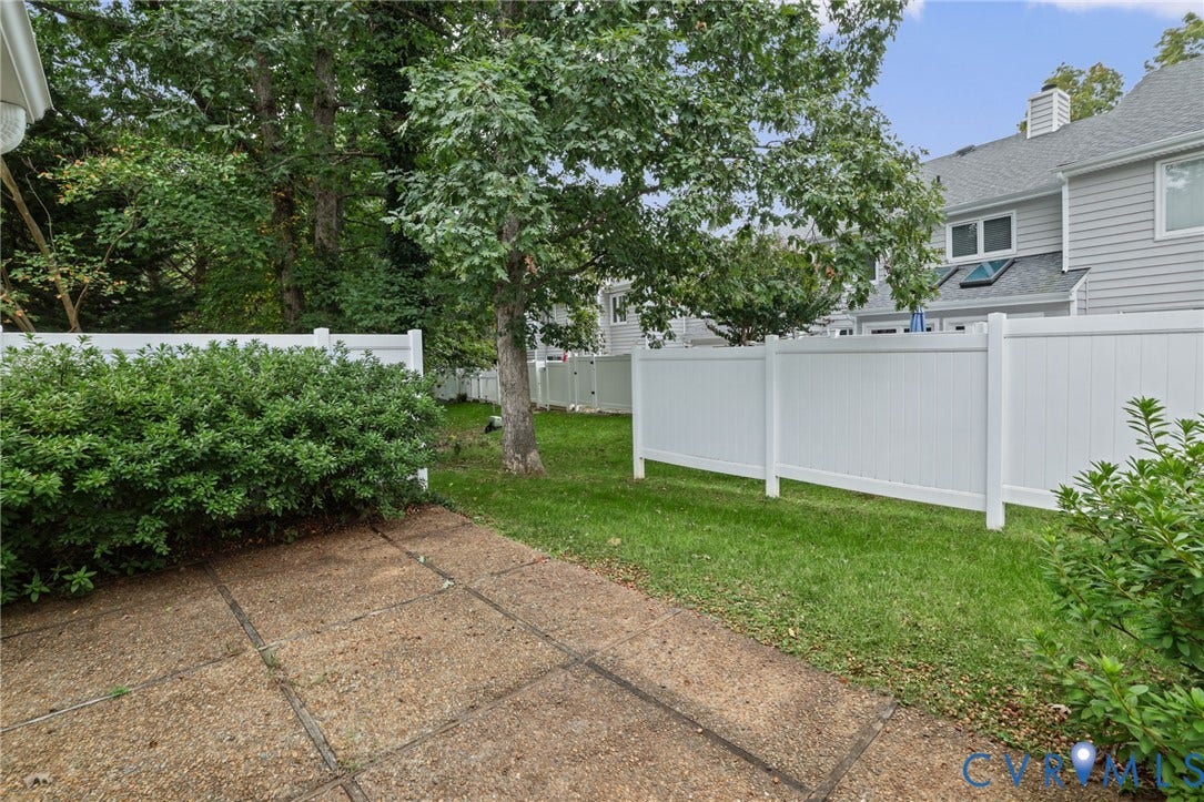1415 Sycamore Mews Circle, Sycamore Mews, Midlothian, VA 23113 Private rear patio featuring aggregate concrete flooring, enclosed by a white vinyl privacy fence and bordered by mature trees and manicured landscaping