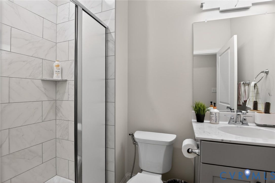 Glen Allen, VA 23059 Bathroom featuring a shower with floor-to-ceiling stone-finish tile surround, a built-in shower niche, a vanity with stone-finish countertop, and a wall-mounted light fixture