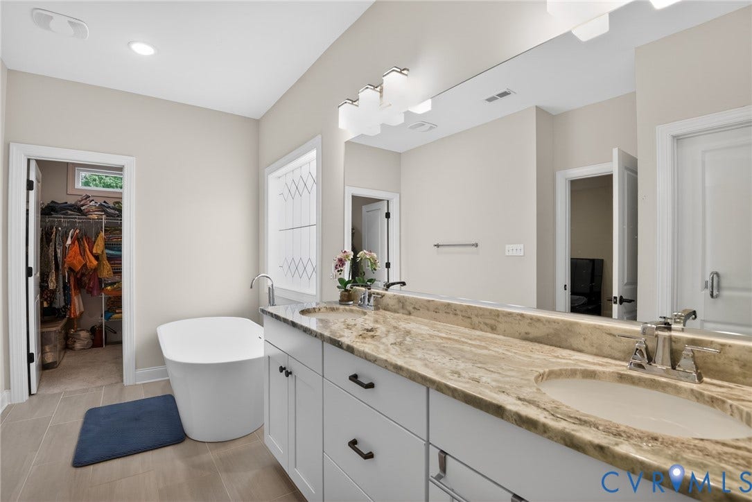Glen Allen, VA 23059 Dual-sink vanity with stone countertop and matte black hardware, freestanding soaking tub, large wall-mounted mirror, and tile flooring