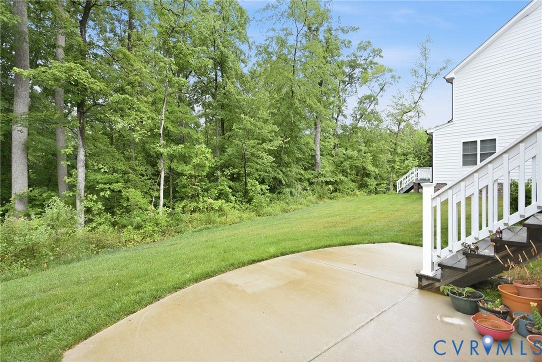 Glen Allen, VA 23059 Rear exterior featuring a concrete patio, white railing, exterior staircase, and a lawn bordering mature woodland