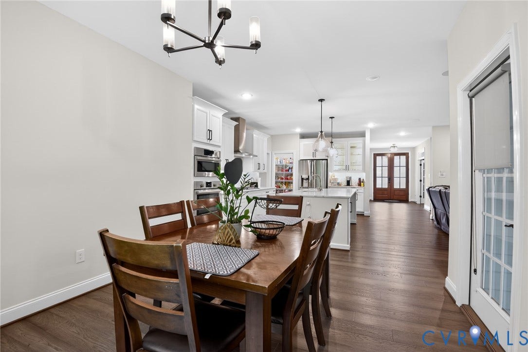Glen Allen, VA 23059 Open-concept kitchen and dining area featuring wood-finish flooring, white shaker cabinetry, stainless steel built-in double wall ovens, a kitchen island with stone countertops, and multi-light pendant chandeliers