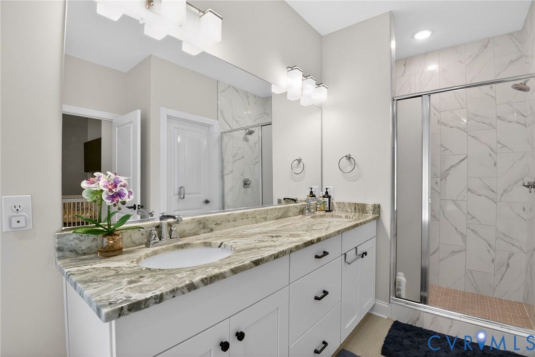 Glen Allen, VA 23059 Dual-sink vanity with stone countertop, white shaker-style cabinetry, matte black hardware, and floor-to-ceiling tile shower enclosure