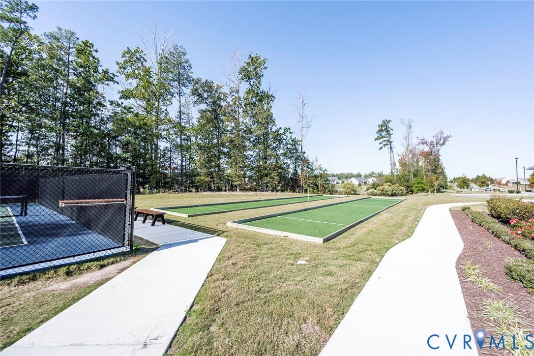 7577 Southamptonshire Way, Autum Pines, New Kent, VA 23124 Outdoor recreation area featuring two bocce ball courts with synthetic turf, perimeter chain-link fencing, concrete walking paths, and mature woodland borders