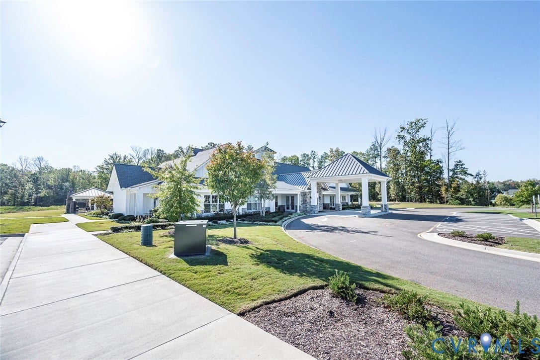 7577 Southamptonshire Way, Autum Pines, New Kent, VA 23124 Exterior featuring a white facade, metal roof accents, covered porte-cochre, paved driveway, and professional landscaping
