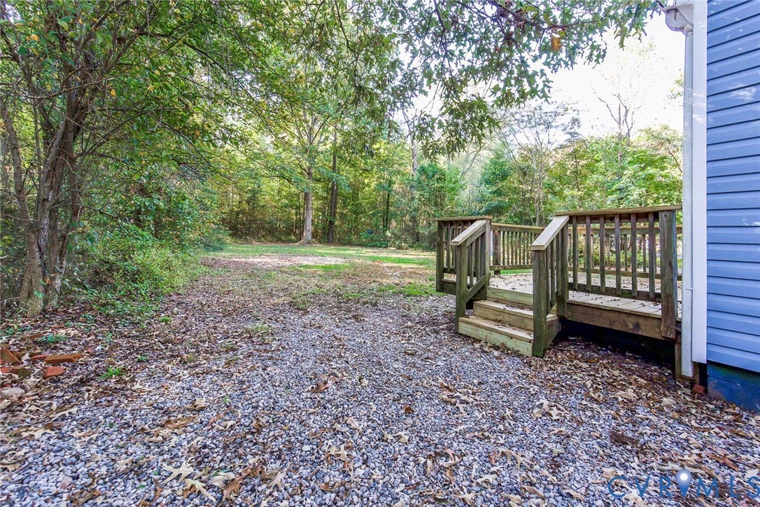 3017 Kingsdale Road, Chesterfield, VA 23237 Backyard featuring a raised wooden deck with railing, gravel ground cover, and surrounding mature trees