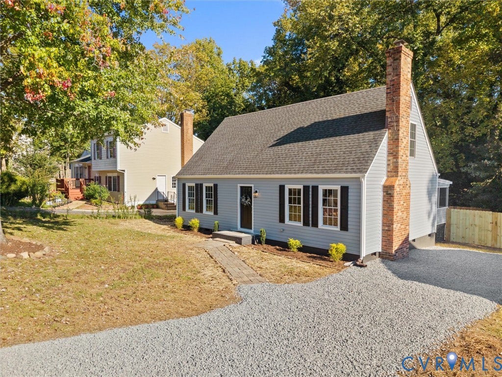 5105 Carryback Drive, Richmond, VA 23234 Cape Cod exterior featuring light-toned vinyl siding, dark shutters, an exposed brick chimney, and a gravel driveway
