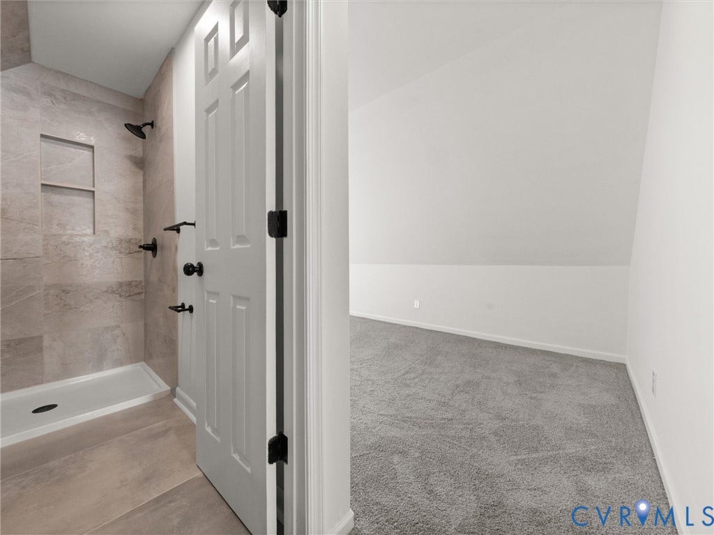 5105 Carryback Drive, Richmond, VA 23234 Walk-in shower featuring large-format tile surround, recessed wall niche, and matte black fixtures, paired with a carpeted room featuring a slanted ceiling