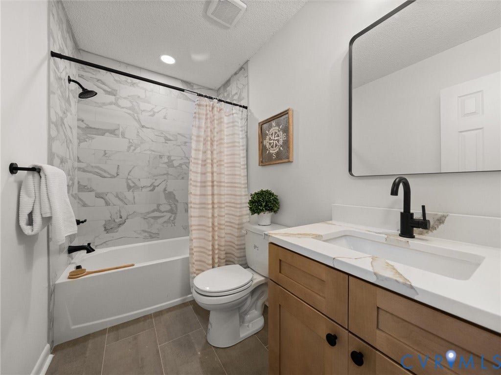 5105 Carryback Drive, Richmond, VA 23234 Bathroom featuring a wood-finish vanity with a stone-top integrated sink, matte black hardware, a rectangular vanity mirror, and a tub-shower combination with full-height stone-patterned tile surround