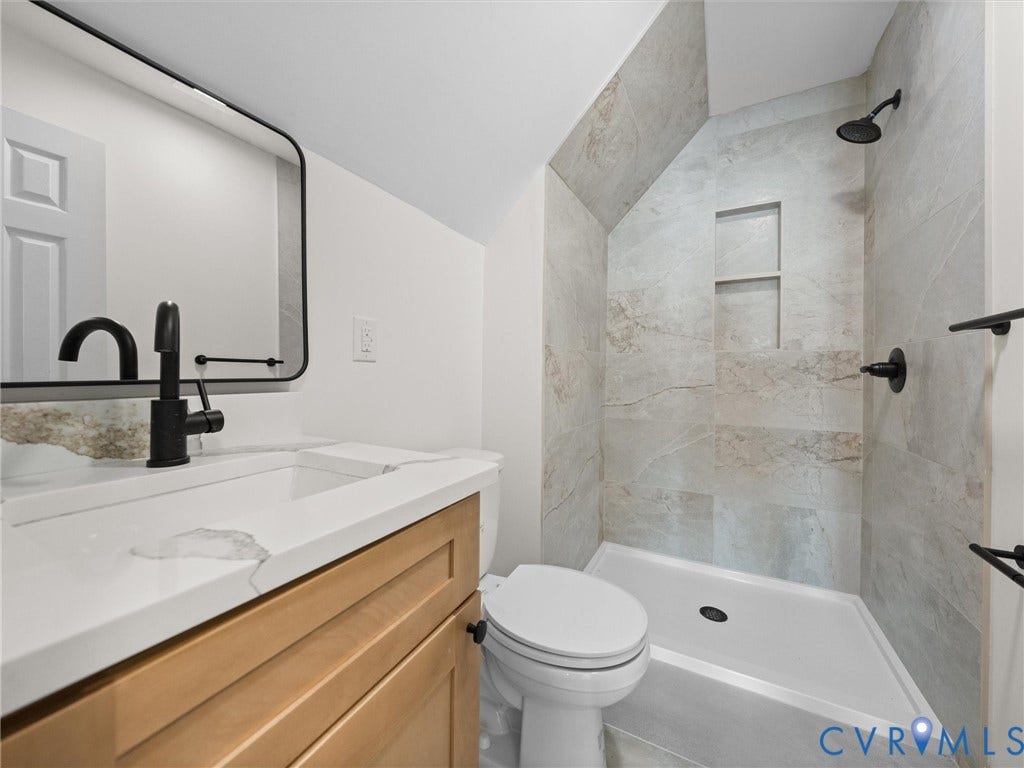 5105 Carryback Drive, Richmond, VA 23234 Bathroom featuring a wood-finish vanity with a stone-top integrated sink, matte black hardware, a framed rectangular mirror, and a walk-in shower with large-format wall tile and a built-in recessed niche