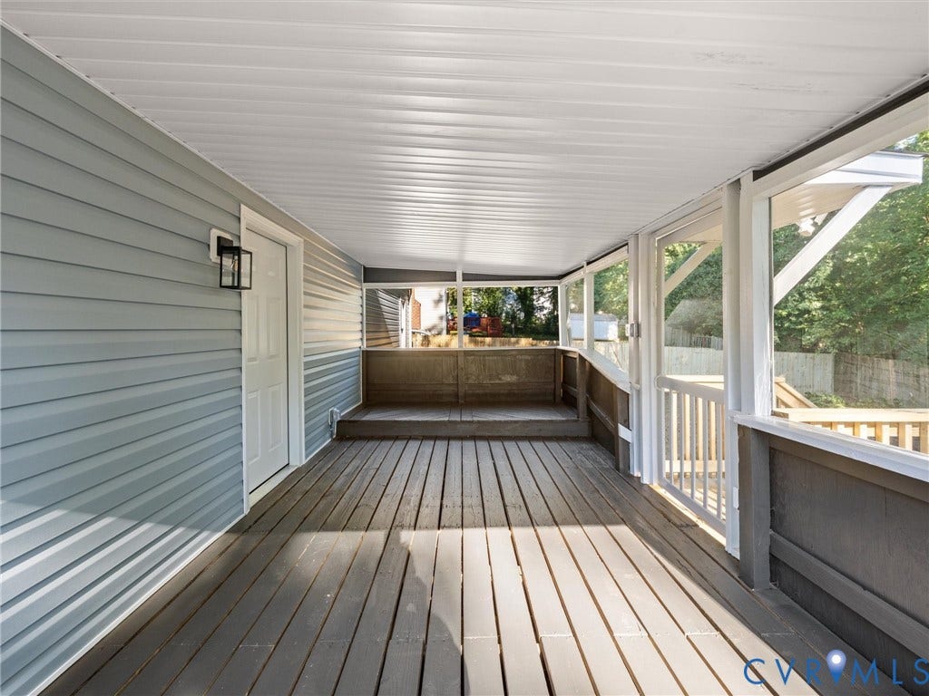 5105 Carryback Drive, Richmond, VA 23234 Covered porch featuring wood-finish decking, light blue vinyl siding, screen enclosure, and wall-mounted exterior lighting
