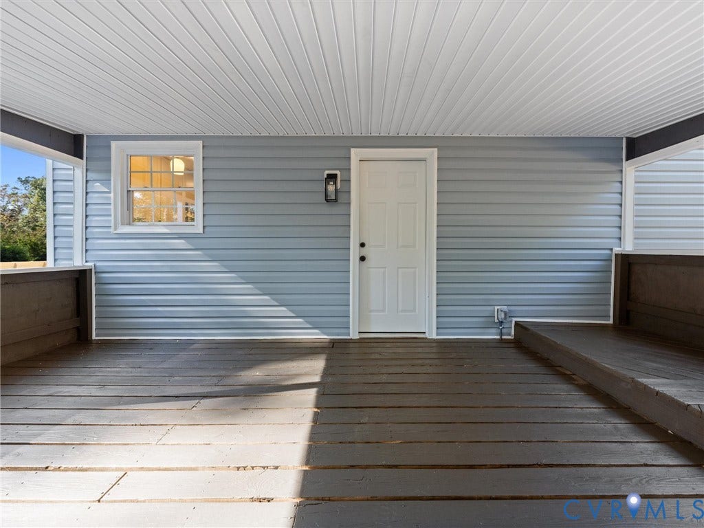 5105 Carryback Drive, Richmond, VA 23234 Covered porch featuring wood-finish decking, light blue horizontal siding, white-trimmed six-panel exterior door, and a wall-mounted light fixture