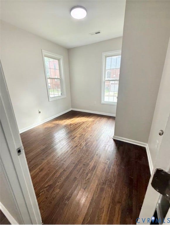 1201 W Broadway, Hopewell, VA 23860 Room featuring wood-finish flooring, neutral wall paint, two windows with white trim, and a flush-mount overhead light fixture