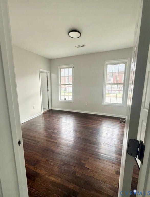 1201 W Broadway, Hopewell, VA 23860 Interior room featuring dark wood-finish flooring, two multi-pane windows, neutral wall paint, and a circular flush-mount ceiling light fixture