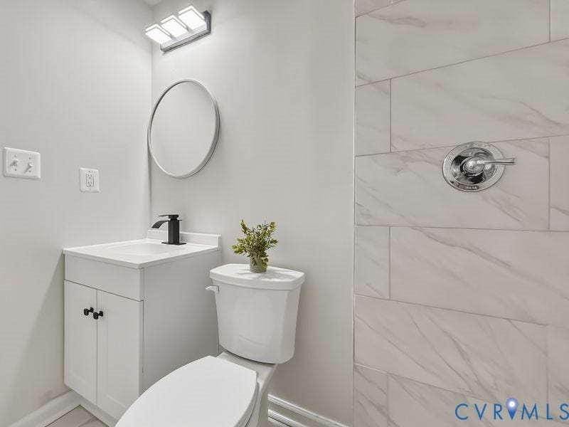 2500 ford Avenue, Richmond, VA 23223 Bathroom featuring a white vanity cabinet, a matte black faucet, a round wall-mounted mirror, three-bulb vanity lighting, and wall tiling with a vein pattern