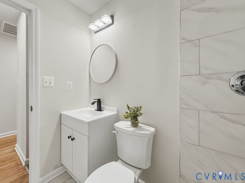 2500 ford Avenue, Richmond, VA 23223 White vanity with a rectangular sink, matte black faucet, round wall-mounted mirror, three-light fixture, and light-toned tile shower surround