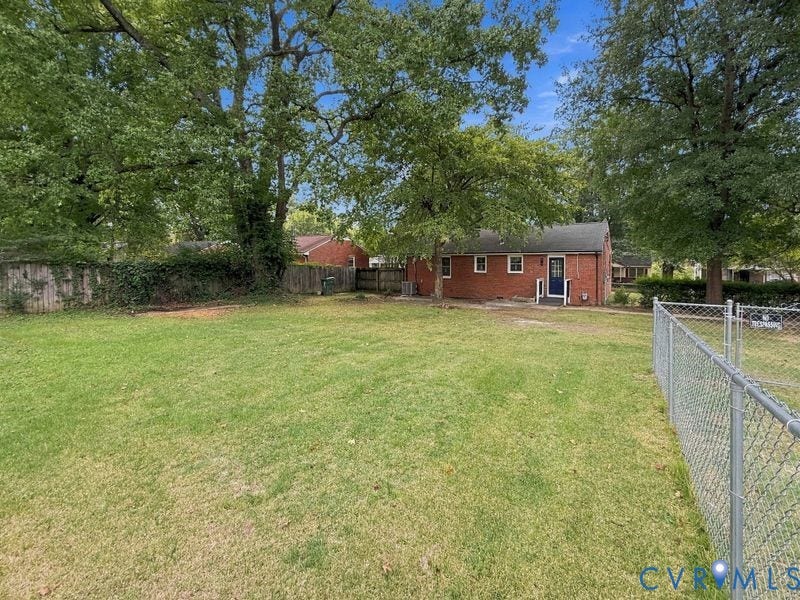 2500 ford Avenue, Richmond, VA 23223 Expansive backyard featuring a large grass lawn, mature trees, wood privacy fencing, and chain-link perimeter enclosure