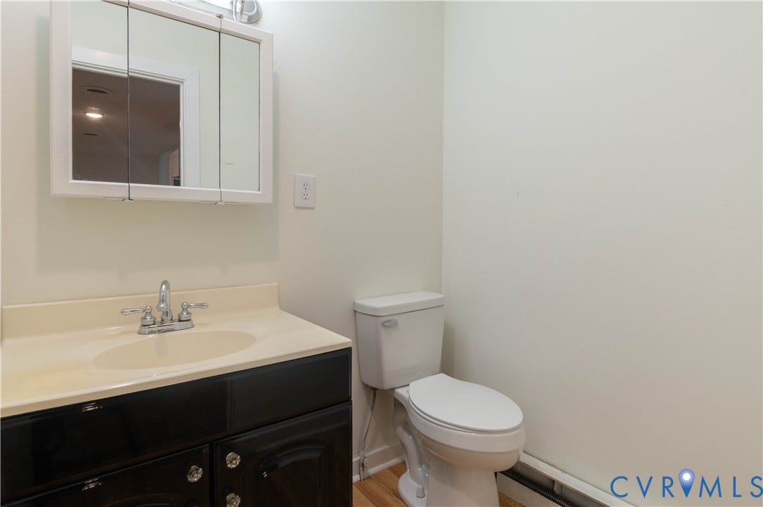 9045 Blounts Corner Road, Smithfield, VA 23430 Dark-toned vanity with a light-toned integrated countertop and basin, dual-handle chrome faucet, three-door mirrored medicine cabinet, and standard porcelain toilet