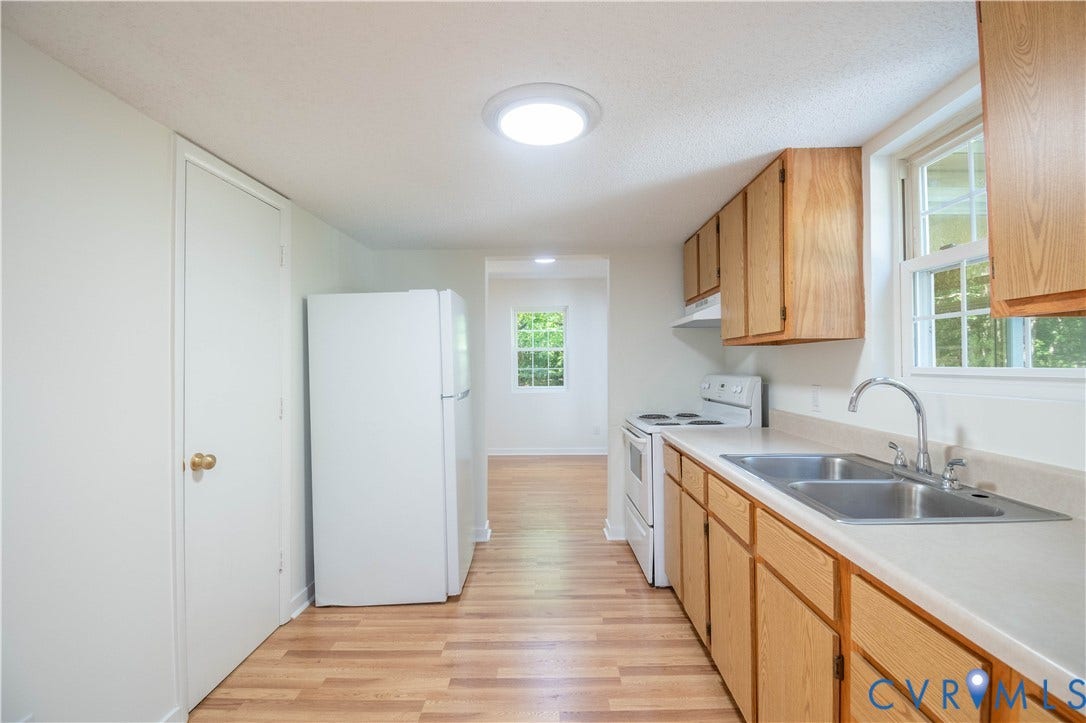9045 Blounts Corner Road, Smithfield, VA 23430 Kitchen featuring wood-finish cabinetry, neutral solid-surface countertops, dual-basin stainless steel sink, wood-finish flooring, and recessed ceiling lighting