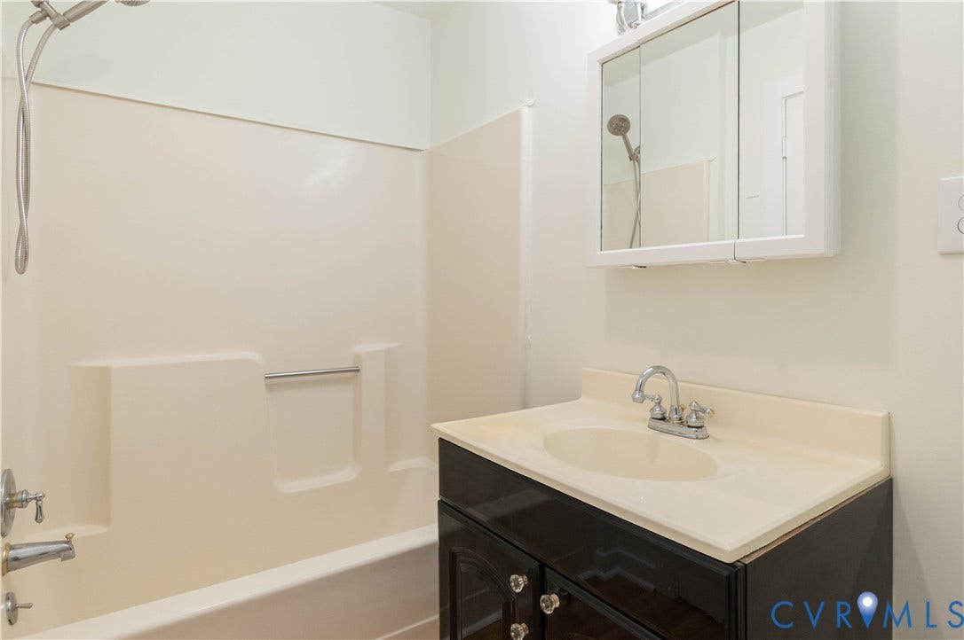 9045 Blounts Corner Road, Smithfield, VA 23430 Bathroom featuring a dark wood-finish vanity, integrated countertop with sink, chrome dual-handle faucet, wall-mounted medicine cabinet, and a bathtub with a shower surround