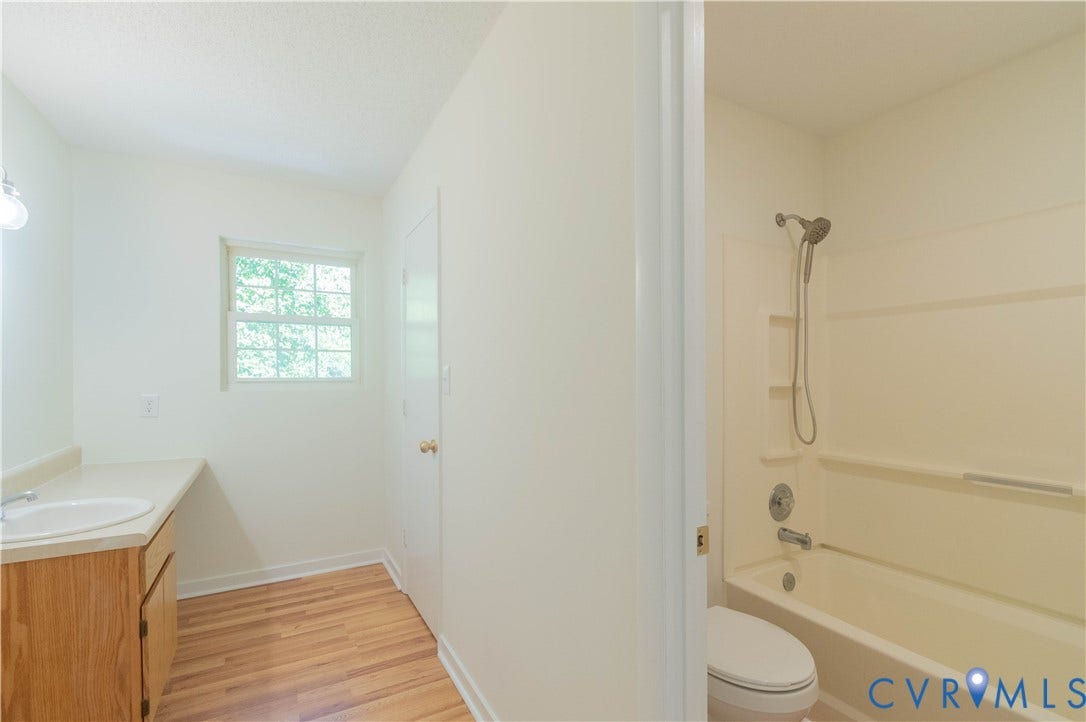 9045 Blounts Corner Road, Smithfield, VA 23430 Bathroom featuring a wood-finish vanity with a drop-in sink, wood-finish flooring, a combination tub and shower with a handheld fixture, and a window providing natural light
