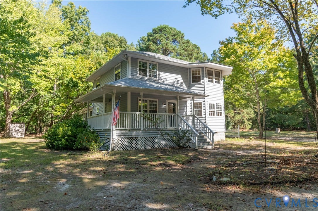 9045 Blounts Corner Road, Smithfield, VA 23430 Two-story residence featuring light gray horizontal siding, a wraparound covered porch with white railing, and lattice skirting, situated on a wooded lot