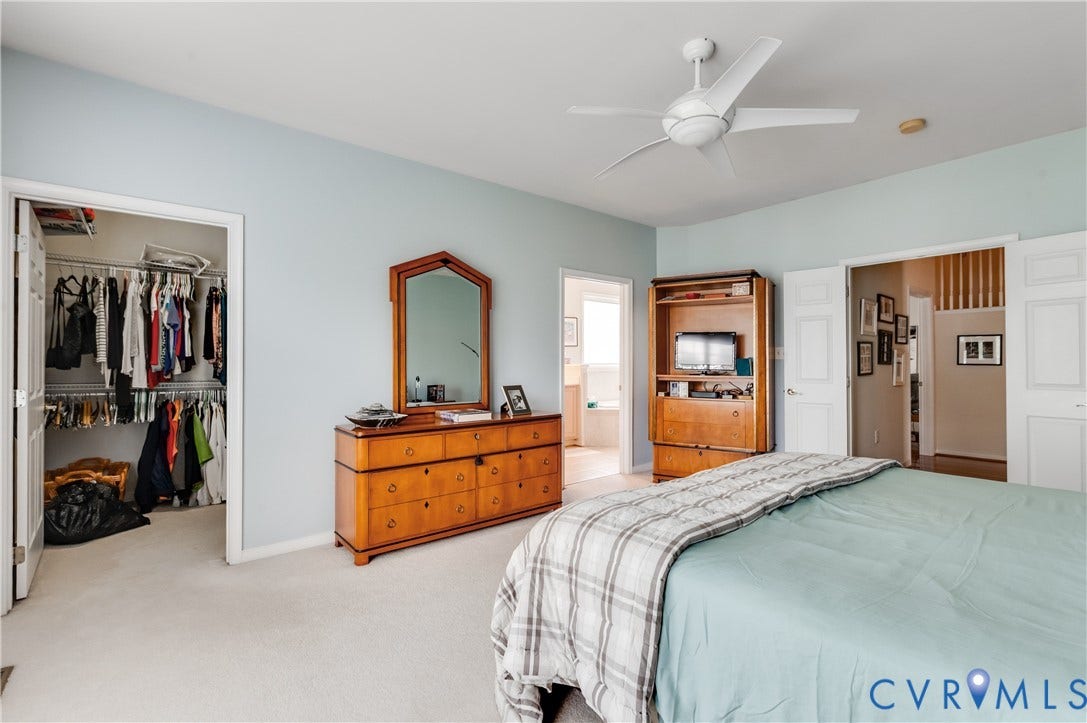 704 Taylors Hill Court, Manakin Sabot, VA 23103 Spacious sleeping area with light blue walls and plush carpeting, featuring a walk-in closet with built-in shelving, a ceiling fan with integrated lighting, and white bi-fold doors