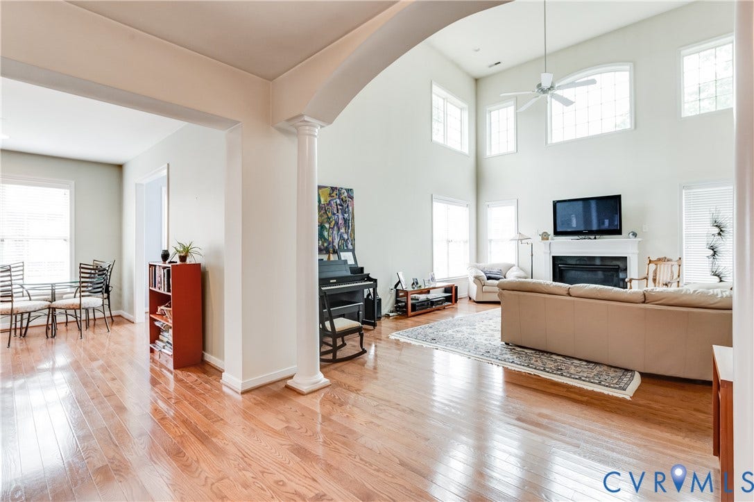 704 Taylors Hill Court, Manakin Sabot, VA 23103 Expansive living area featuring soaring ceilings, wood-finish flooring, a fireplace with a white mantel, arched doorways, and numerous transom windows