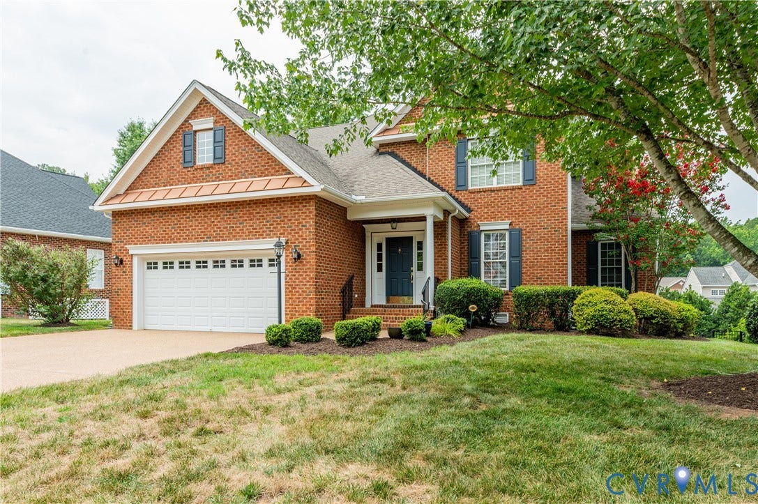704 Taylors Hill Court, Manakin Sabot, VA 23103 Brick exterior with white garage door, dark blue shutters, covered front porch, and mature landscaping