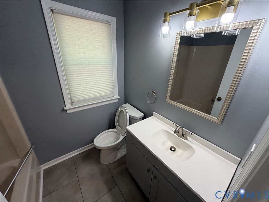 2228 Early Settlers Road, Midlothian, VA 23235 Hall Bathroom Vanity featuring a solid-surface countertop with an integrated basin, grey cabinetry, three-light metal fixture, framed wall mirror, and large-format tile flooring