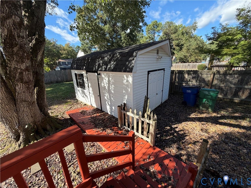 2228 Early Settlers Road, Midlothian, VA 23235 Detached storage structure featuring white vinyl siding, a black asphalt shingle gambrel roof, and double-door entry, complemented by a wood-finish deck and perimeter wood fencing