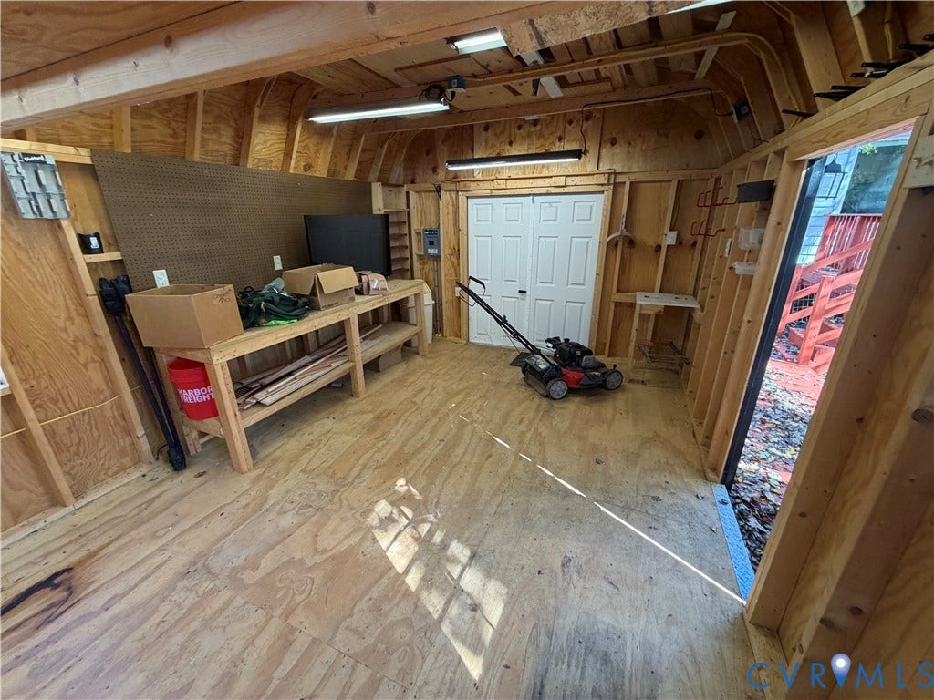 2228 Early Settlers Road, Midlothian, VA 23235 Outbuilding featuring exposed wood-stud framing, plywood flooring, pegboard wall panels, built-in wooden workbench, and dual-tube lighting fixtures