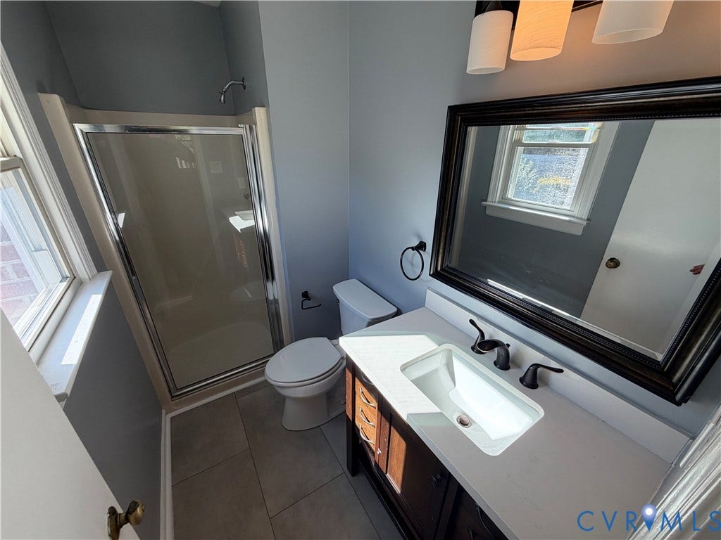 2228 Early Settlers Road, Midlothian, VA 23235 Bathroom featuring a vanity with a light-toned countertop, undermount sink, and dark wood-finish cabinetry, paired with a glass-enclosed shower, large-format tile flooring, and a framed wall mirror
