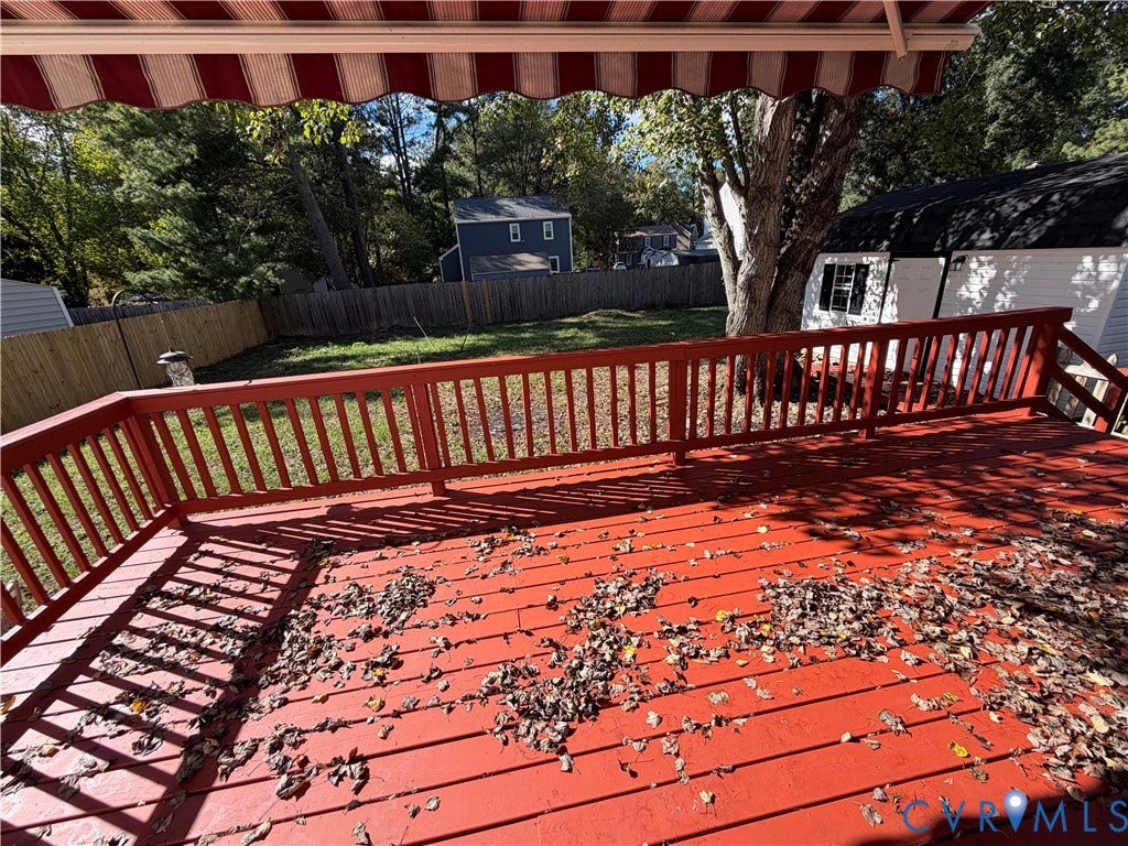 2228 Early Settlers Road, Midlothian, VA 23235 Raised wooden deck with a red-painted finish, wooden balustrade, retractable striped fabric awning, fenced backyard, and a detached outbuilding