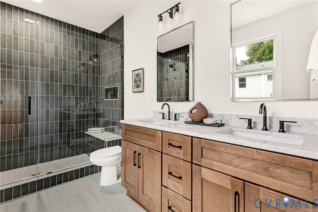 3021 E Franklin Street, St. John's Church, Richmond, VA 23223 Double vanity with stone countertop and undermount sinks, wood-finish cabinetry, matte black plumbing fixtures, walk-in shower with vertical tile surround and integrated bench, and rectangular wall-mounted mirrors
