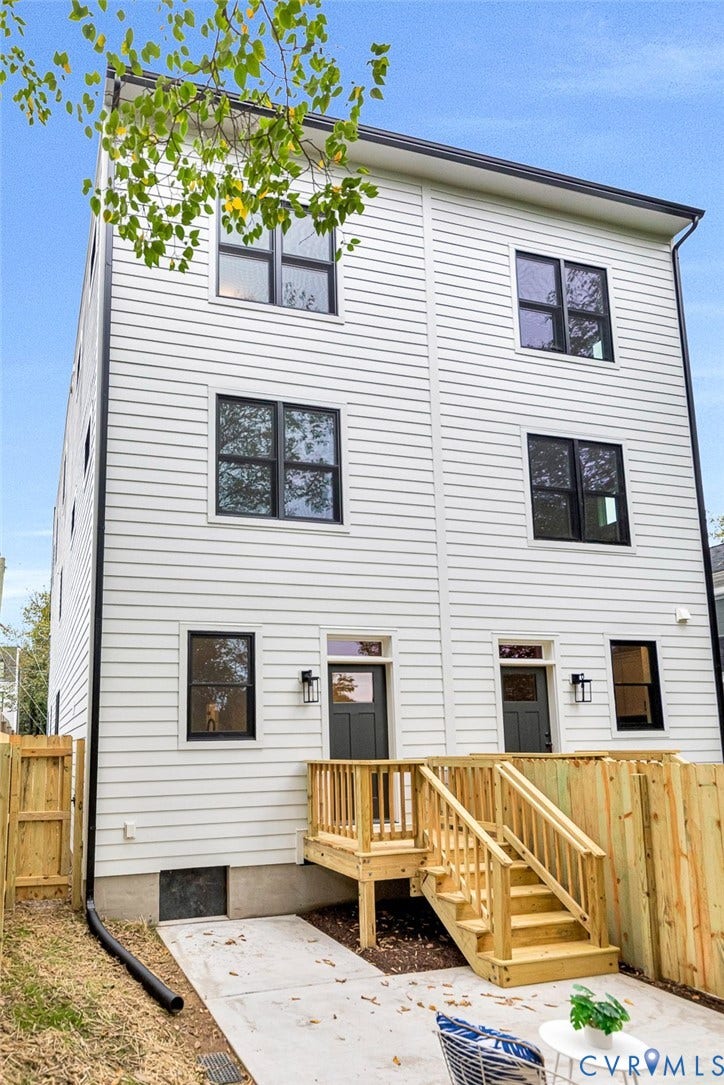 3021 E Franklin Street, St. John's Church, Richmond, VA 23223 Three-story horizontal lap siding exterior with black-framed windows, two rear entry doors, wall-mounted exterior lanterns, and a wood deck with stairs leading to a concrete patio