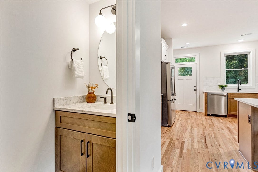 3021 E Franklin Street, St. John's Church, Richmond, VA 23223 Half-bath featuring a vanity with stone-finish countertop, integrated sink, and circular mirror, along with wood-finish flooring extending into the kitchen area