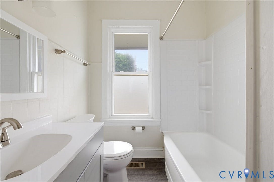 100 N 3rd Avenue, Hopewell, VA 23860 Bathroom featuring a vanity with an integrated basin, white tile tub surround with built-in shelving, dark wood-finish flooring, a framed wall mirror, and brushed metal fixtures