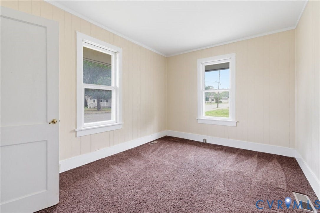 100 N 3rd Avenue, Hopewell, VA 23860 Neutral-toned vertical paneling, wall-to-wall carpeting, two double-hung windows with white trim, and a classic four-panel interior door