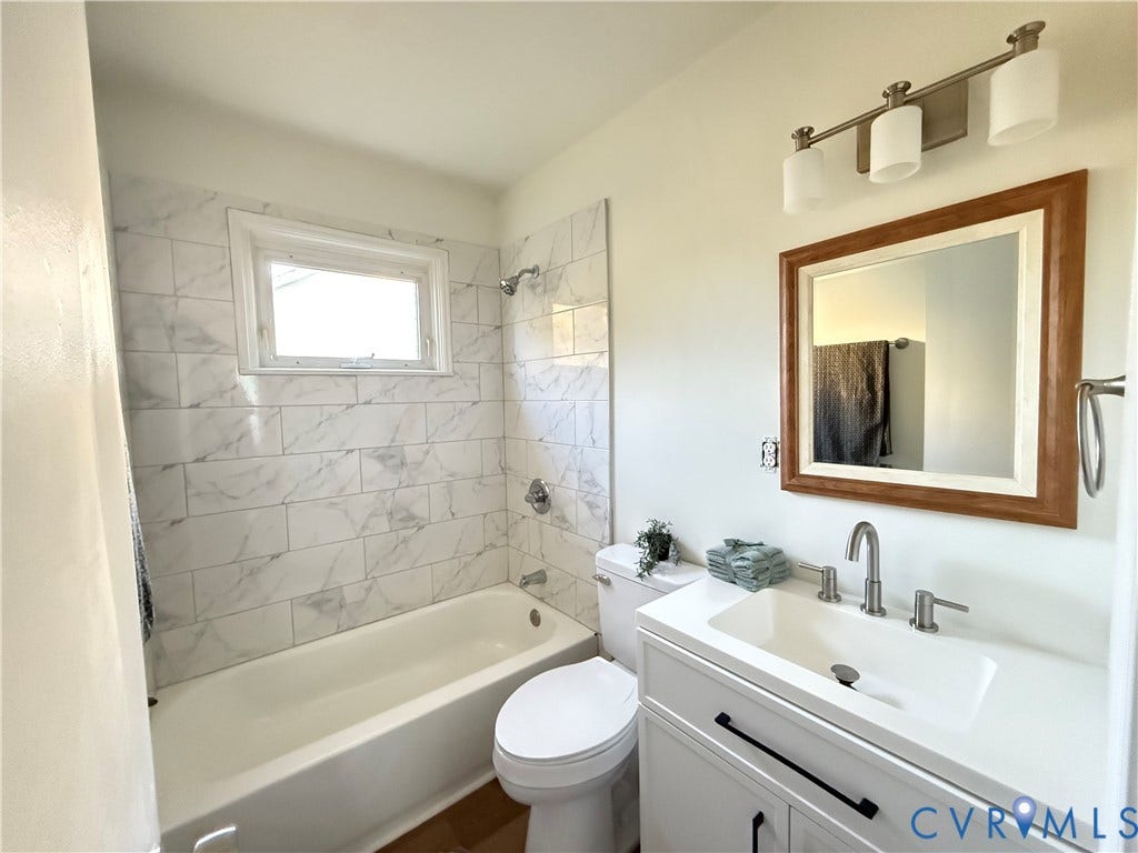 120 N New Avenue, Henrico, VA 23075 Bathroom featuring a white vanity with an integrated basin, white subway tile shower surround with stone-patterned finish, three-light wall-mounted fixture, and a framed mirror