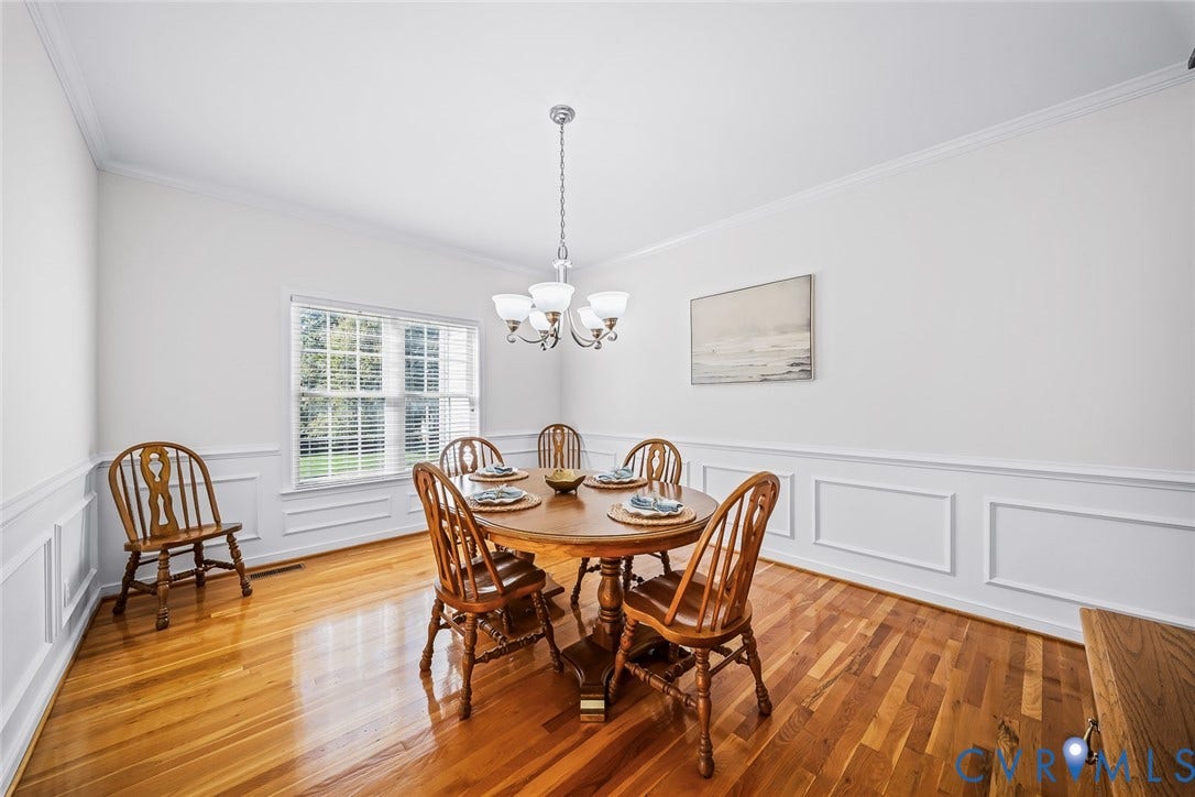 Dining area featuring hard wood flooring, white wainscoting, and a central five-light chandelier