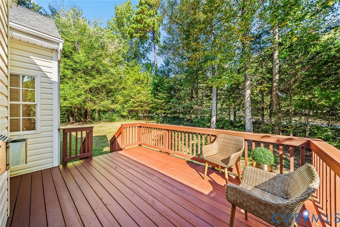 Elevated wooden deck featuring horizontal railings, light-colored vinyl siding, and natural tree coverage