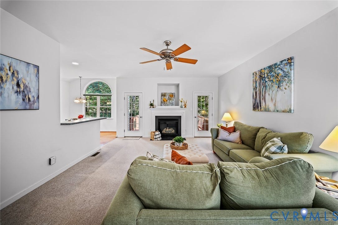 Living area featuring a fireplace with a recessed hearth, arched window, dual glass-paned exterior doors, and a ceiling fan