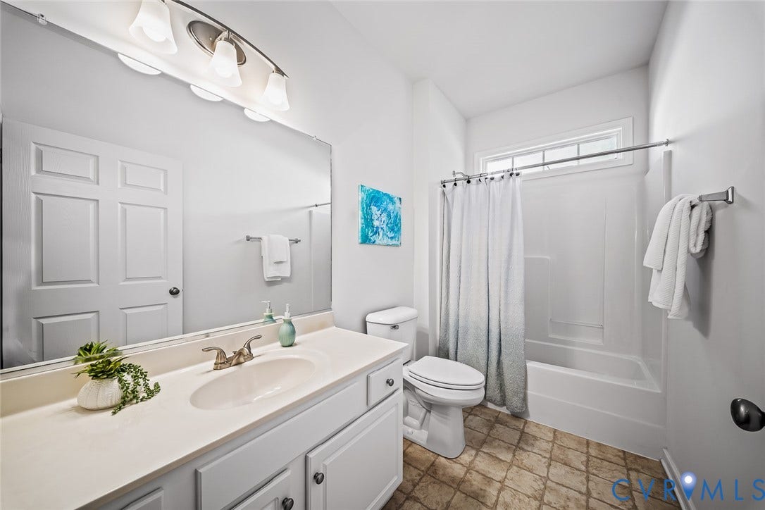 Full-width vanity with an integrated basin, large wall-mounted mirror, multi-bulb overhead lighting, and a bathtub-shower combination with a transom window