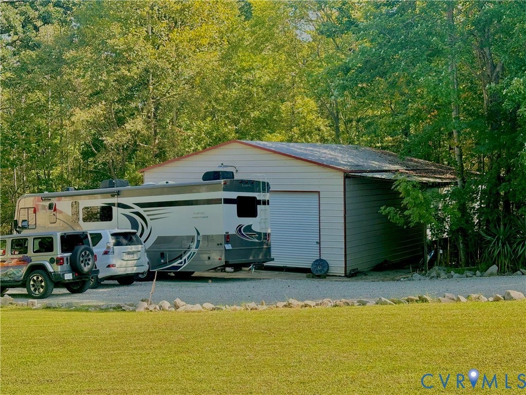 25400 SAYLERS CREEK ROAD, Deatonville, Jetersville, VA 23083 Detached metal-sided garage featuring a roll-up door, gravel parking area, and mature surrounding trees