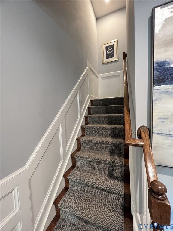 2310 Liesfeld Parkway, West Broad Village, Henrico, VA 23060 Staircase featuring white wainscoting, wooden handrail with a decorative newel post, and patterned carpet runner over wood-finish treads