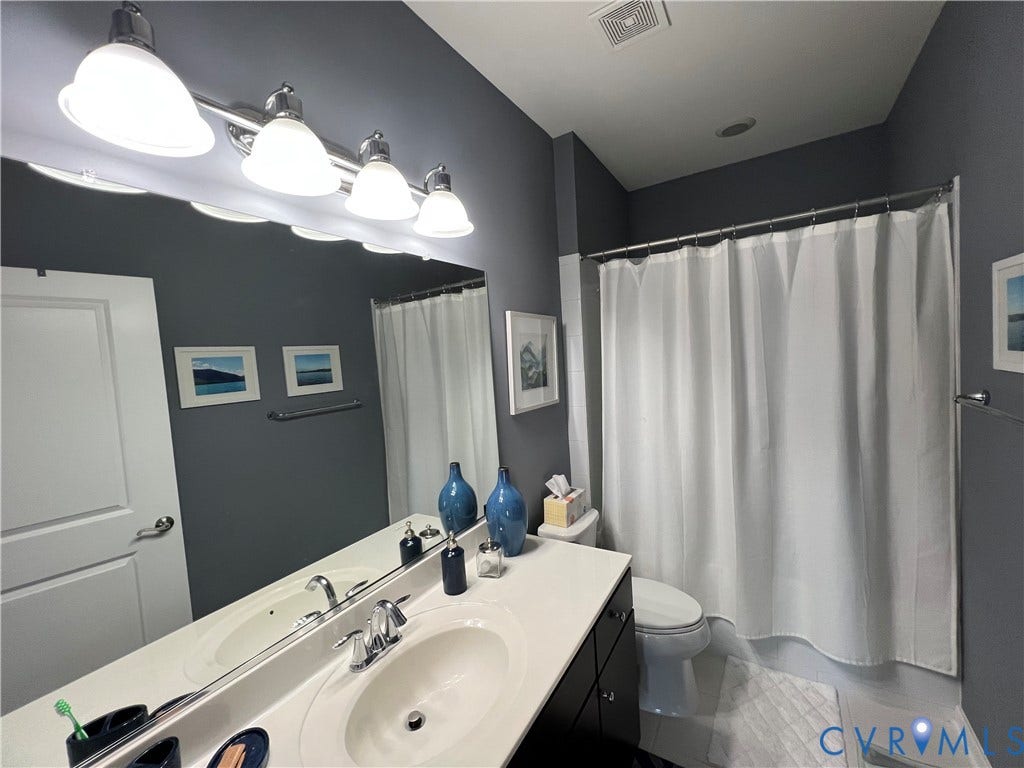 2310 Liesfeld Parkway, West Broad Village, Henrico, VA 23060 Vanity with a solid-surface countertop and integrated sink, four-light vanity fixture, expansive wall-mounted mirror, and a tub-shower combination with a shower rod