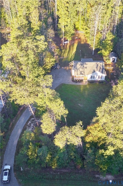 444 Tillar Lane, Mineral, VA 23117 Aerial view of a residential property featuring a gravel driveway, expansive lawn, detached storage structure, and perimeter fencing, all situated within a mature wooded setting