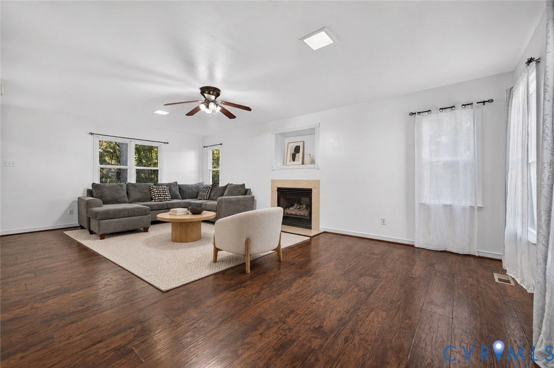 7225 Hartsdale Court, Chesterfield, VA 23832 Virtually-Staged Living area featuring dark wood-finish flooring, a fireplace with a light-toned stone surround, a recessed wall niche, and a central ceiling fan with integrated lighting