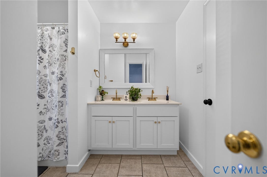7225 Hartsdale Court, Chesterfield, VA 23832 Dual-sink vanity with white shaker-style cabinetry, neutral-toned countertop, brass-finish fixtures, and a framed vanity mirror with coordinating three-light fixture