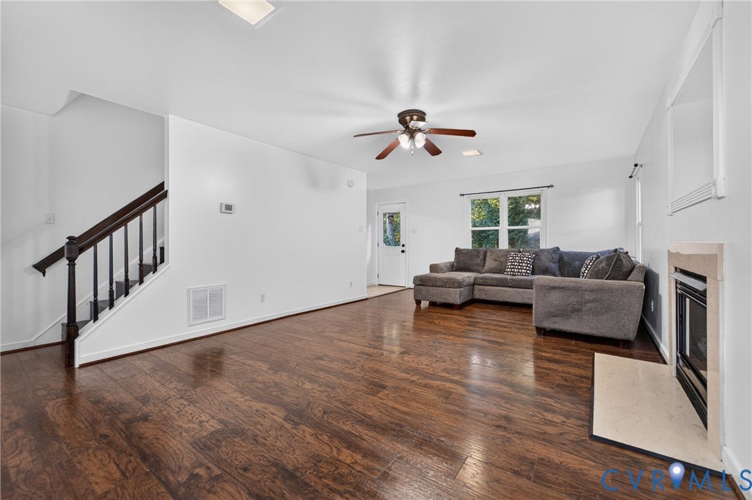 7225 Hartsdale Court, Chesterfield, VA 23832 Living area featuring wood-finish flooring, a fireplace with a stone-surround hearth, a ceiling fan with integrated lighting, and a staircase with a dark wood handrail